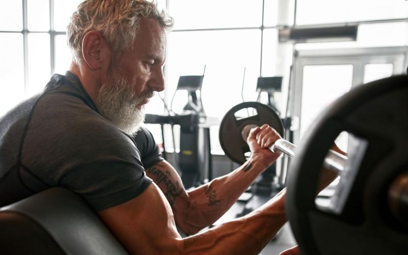 Fit older man doing seated bicep curls in the gym.