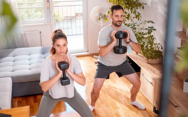 Fit couple doing a dumbbell workout in the their living room.