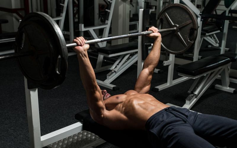 Shirtless muscular man doing a barbell bench press in the gym.